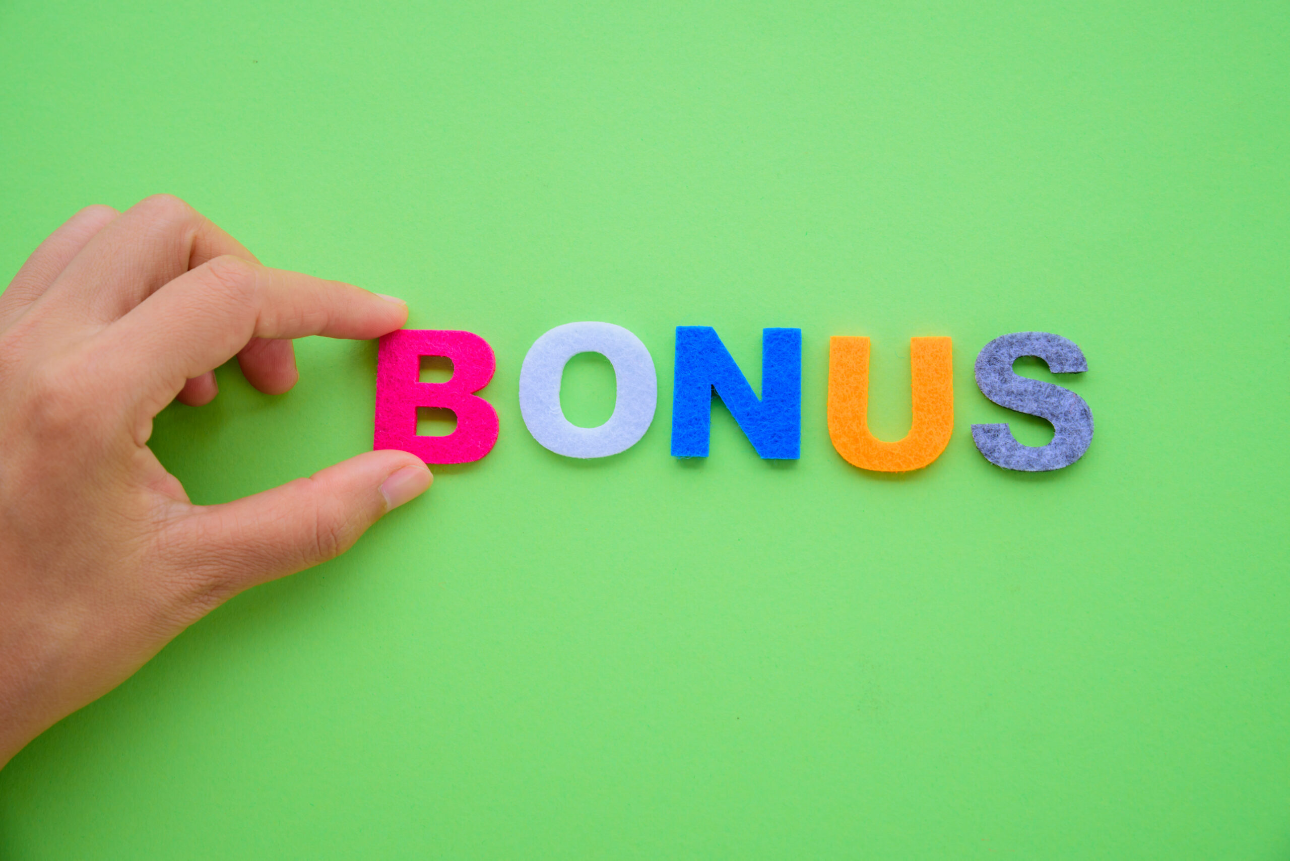 Abstract hand arrange BONUS alphabets word on green background.